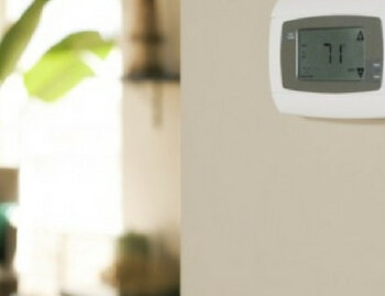 Air conditioning thermostat mounted on wall displaying seventy one degrees