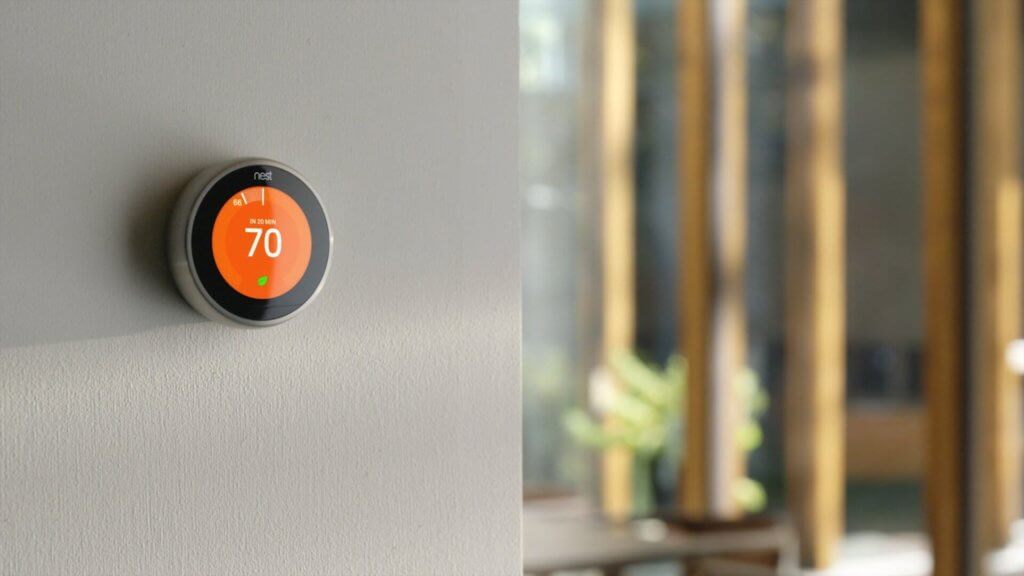 Orange smart thermostat mounted on wall displaying seventy degrees fahrenheit